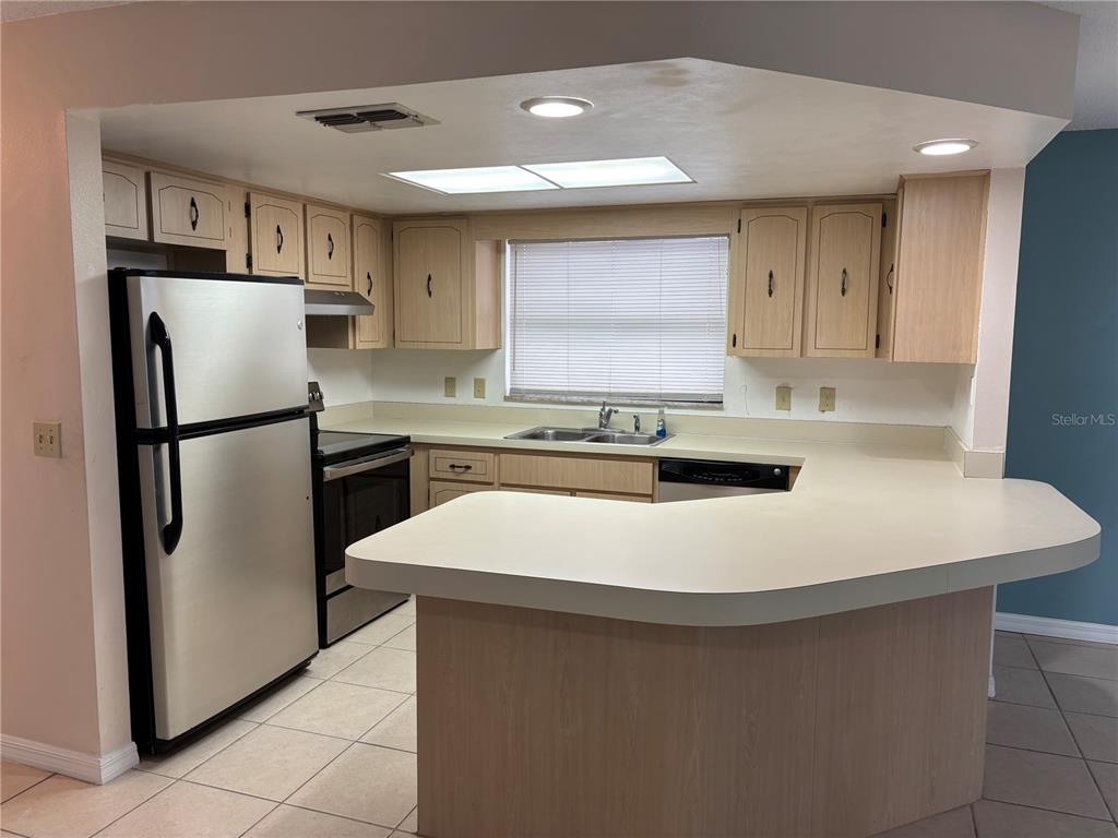 A kitchen features light wood cabinets, a stainless steel refrigerator, and a curved peninsula countertop — 7619 VIENNA LANE, PORT RICHEY, FL