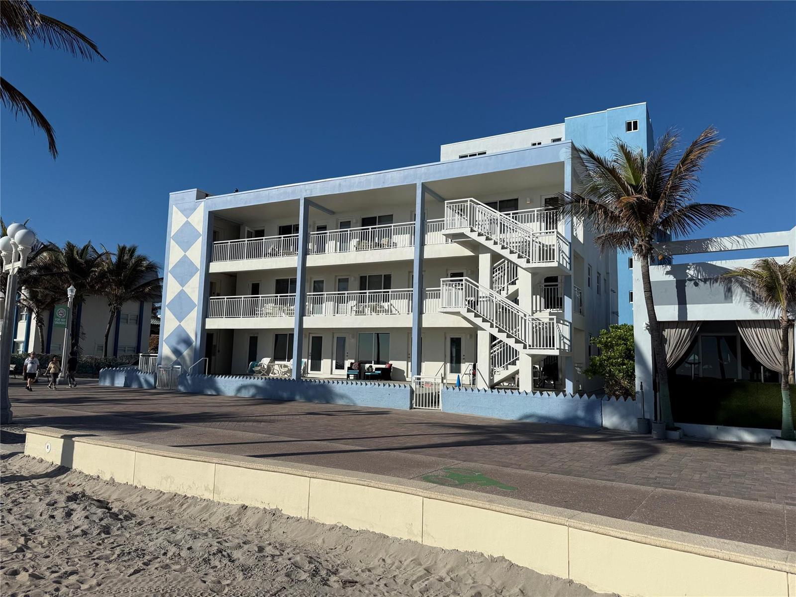 A three-story blue and white beachfront apartment building features exterior staircases and a paved walkway — 310 S Broadwalk # 3b, Hollywood FL 33019, HOLLYWOOD, FL