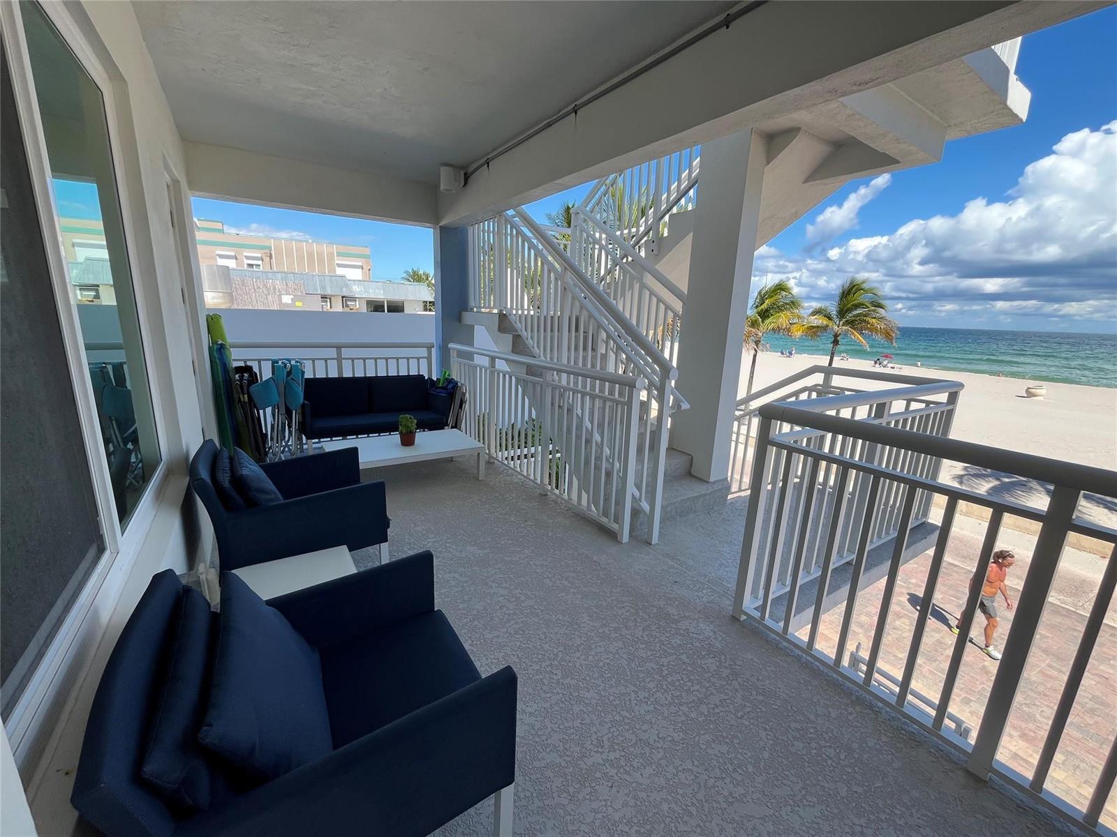 A covered balcony features dark blue outdoor furniture, a white table, and a staircase overlooking the beach — 310 S Broadwalk # 3b, Hollywood FL 33019, HOLLYWOOD, FL