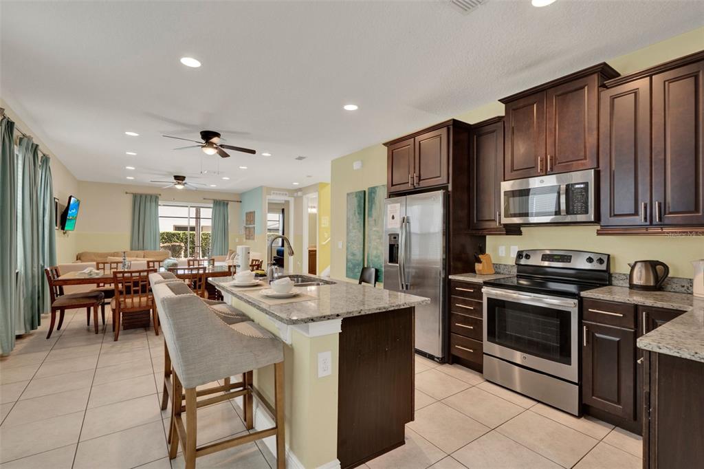 A kitchen with dark wood cabinets, granite countertops, and stainless steel appliances overlooks a dining area — 7613 BROOKHURST LANE, KISSIMMEE, FL