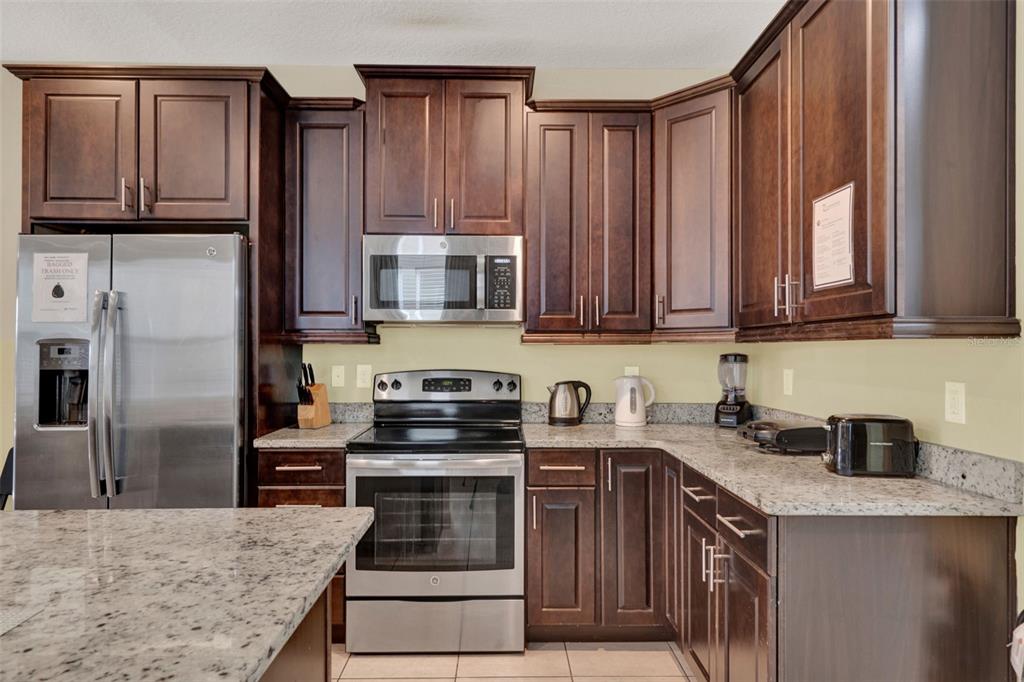 A kitchen features dark wood cabinets, stainless steel appliances, and speckled granite countertops — 7613 BROOKHURST LANE, KISSIMMEE, FL