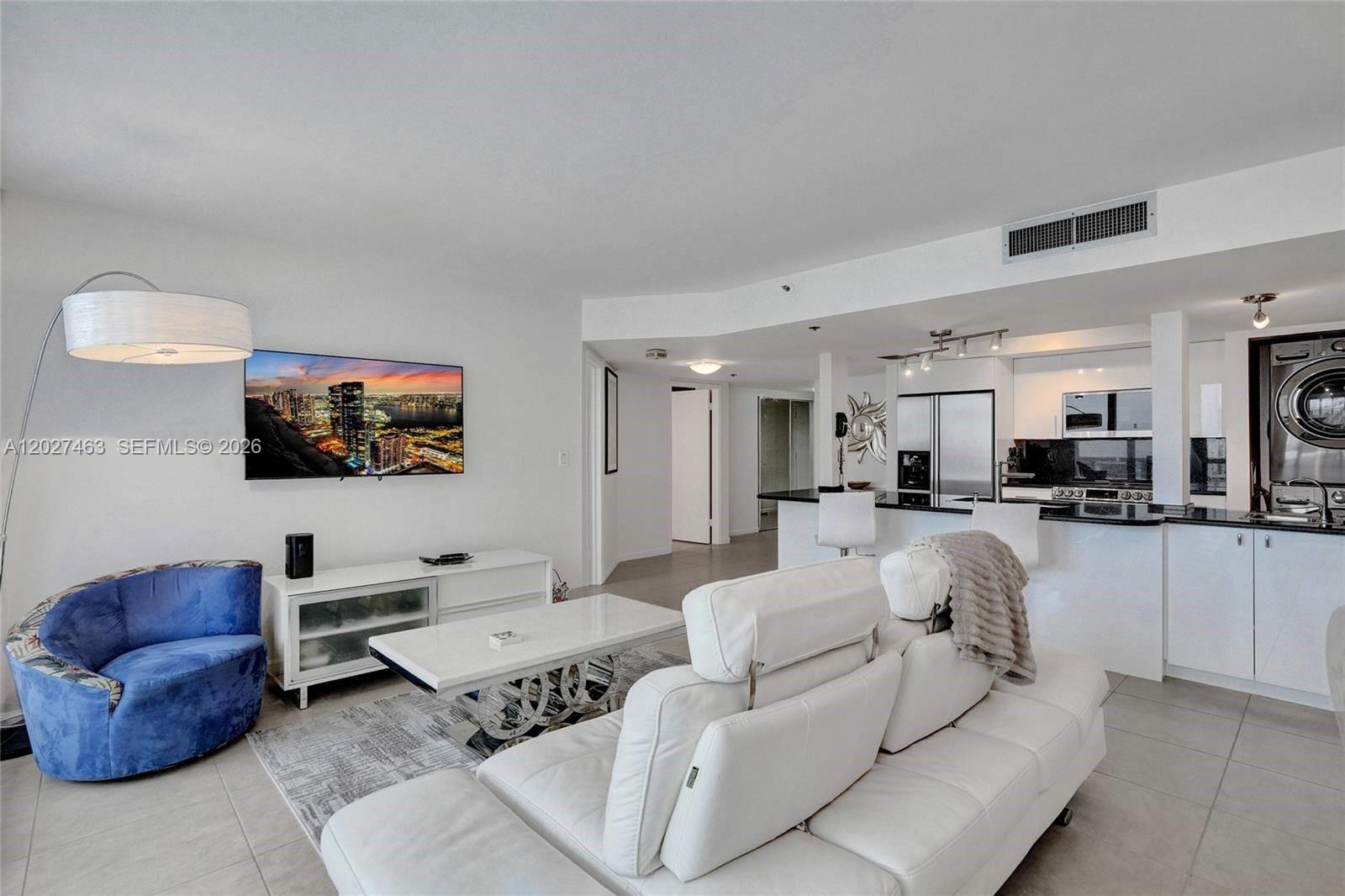 A living room with a white sofa, blue chair, and an open kitchen with appliances — 1717 N Bayshore Dr # 2440, Miami FL 33132, MIAMI, FL