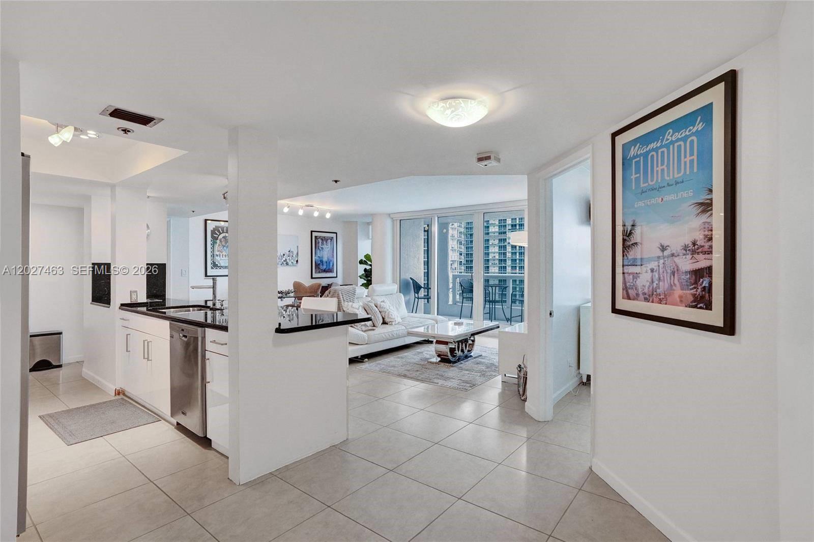 A kitchen with white cabinets and black countertops opens into a living room with balcony access — 1717 N Bayshore Dr # 2440, Miami FL 33132, MIAMI, FL