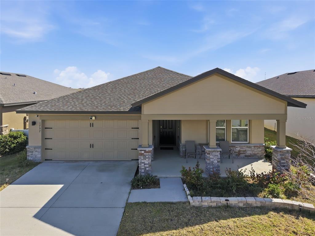 A single-story house with a two-car garage, stone accents, and a covered front porch — 1797 SUNDANCE CHASE ROAD, MINNEOLA, FL