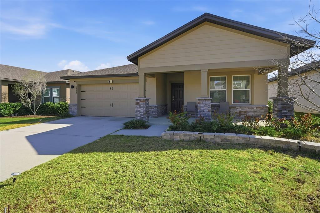 A single-story house with a tan exterior, stone accents, a two-car garage, and a porch — 1797 SUNDANCE CHASE ROAD, MINNEOLA, FL