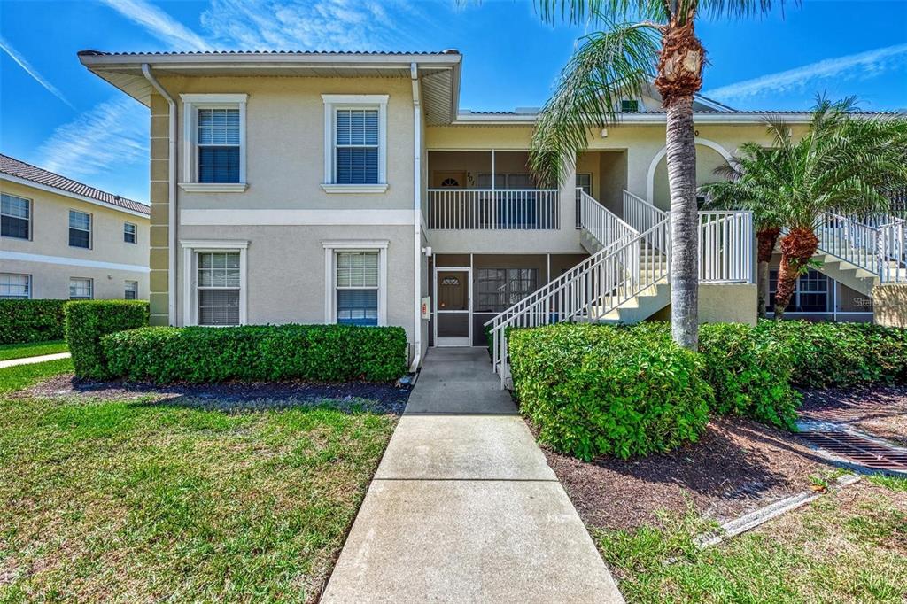 A two-story apartment building exterior features a concrete walkway, a screened entrance, and outdoor stairs — 400 MIRABELLA CIRCLE UNIT 201, VENICE, FL