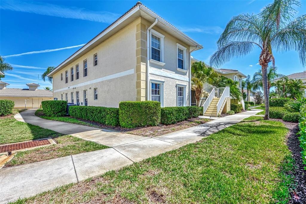 A two-story stucco apartment building with a staircase and concrete walkways on a sunny day — 400 MIRABELLA CIRCLE UNIT 201, VENICE, FL