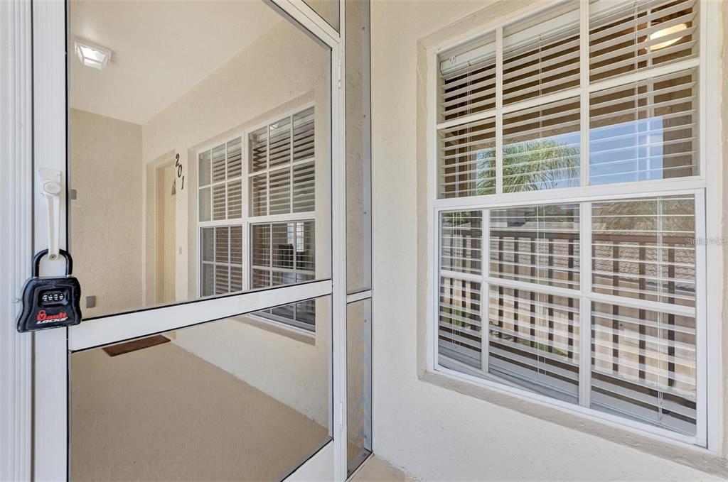 A view of a covered entryway featuring a screen door with a lockbox and windows — 400 MIRABELLA CIRCLE UNIT 201, VENICE, FL
