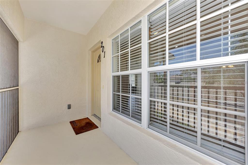 A covered entryway features a beige door, a small welcome mat, and large grid windows — 400 MIRABELLA CIRCLE UNIT 201, VENICE, FL