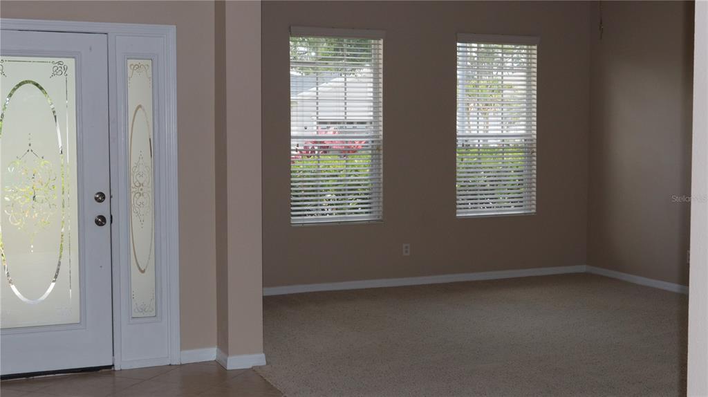 A carpeted room features two windows with blinds and a white front door with glass — 2552 HOBBLEBRUSH DRIVE, NORTH PORT, FL