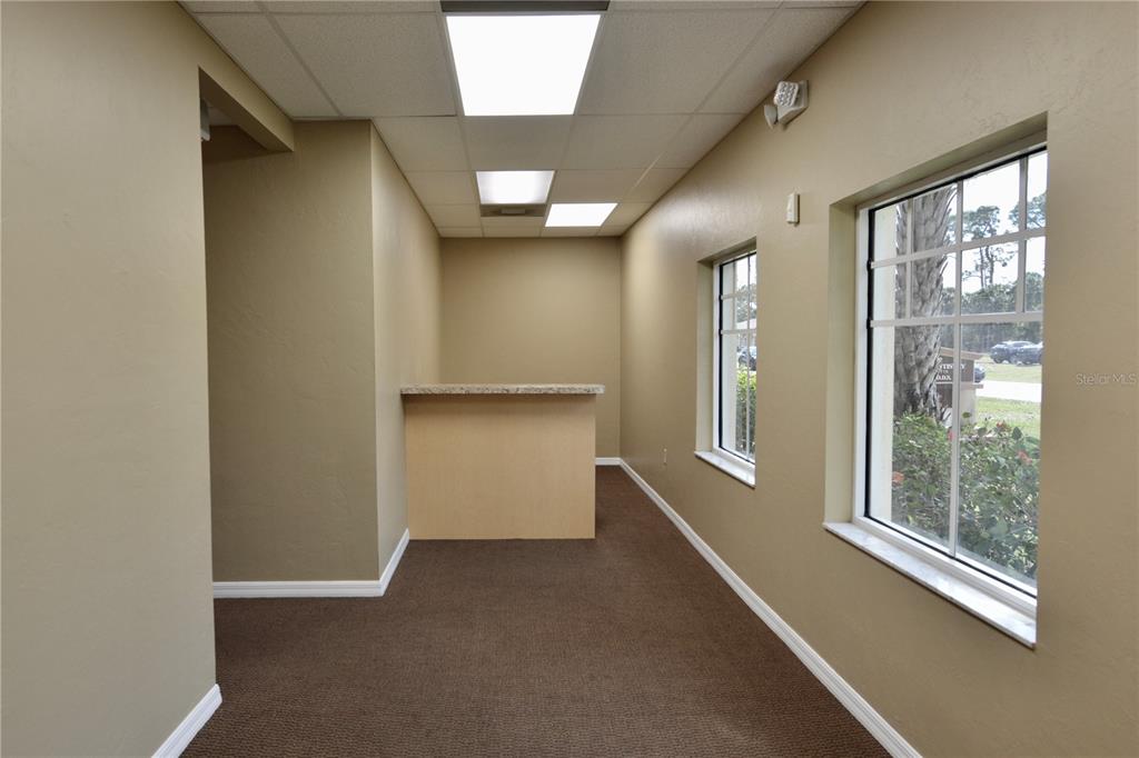 An office space features tan walls, brown carpeting, a built-in counter, and two windows — 2496 CARING WAY UNIT B, PORT CHARLOTTE, FL