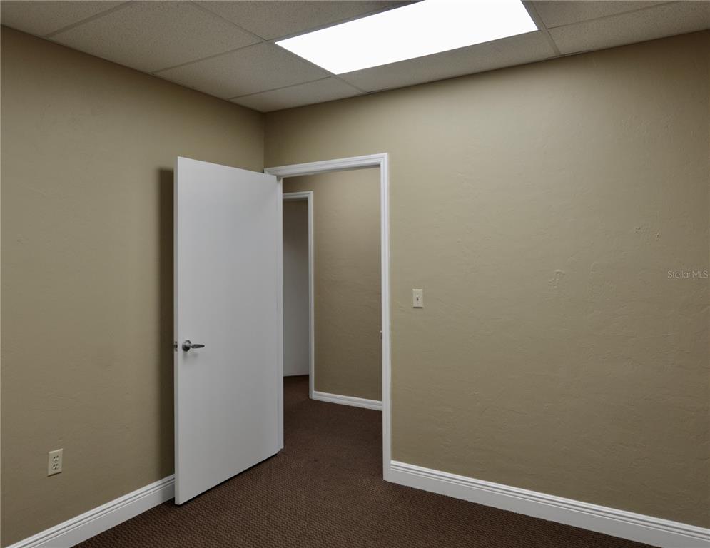 An interior room with tan walls, brown carpeting, a white door, and a drop ceiling — 2496 CARING WAY UNIT B, PORT CHARLOTTE, FL