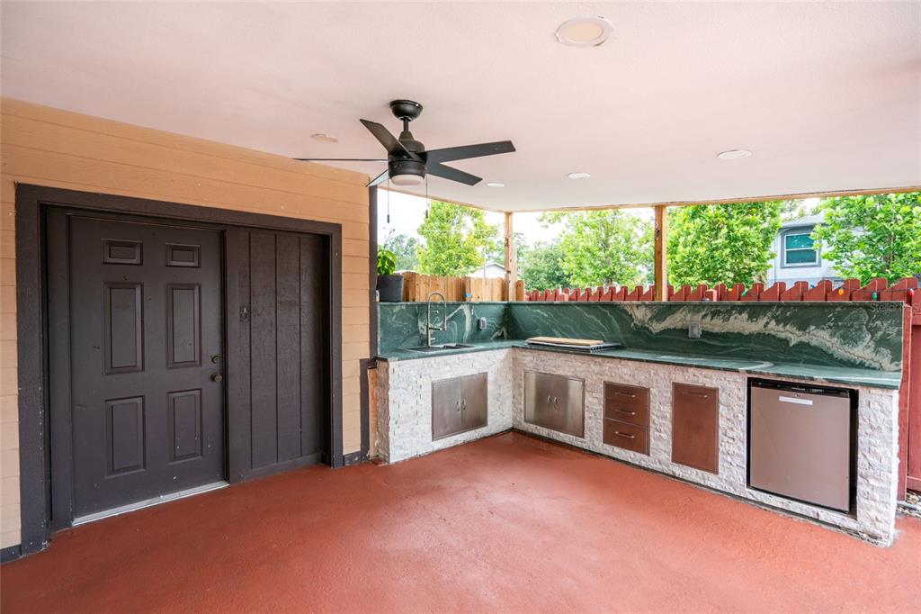 A covered outdoor patio features a stone-faced kitchen island with a sink and stainless appliances — 9241 N 52ND STREET, TAMPA, FL