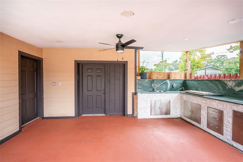 A covered outdoor patio features a built-in kitchen with stone counters and dark doors — 9241 N 52ND STREET, TAMPA, FL