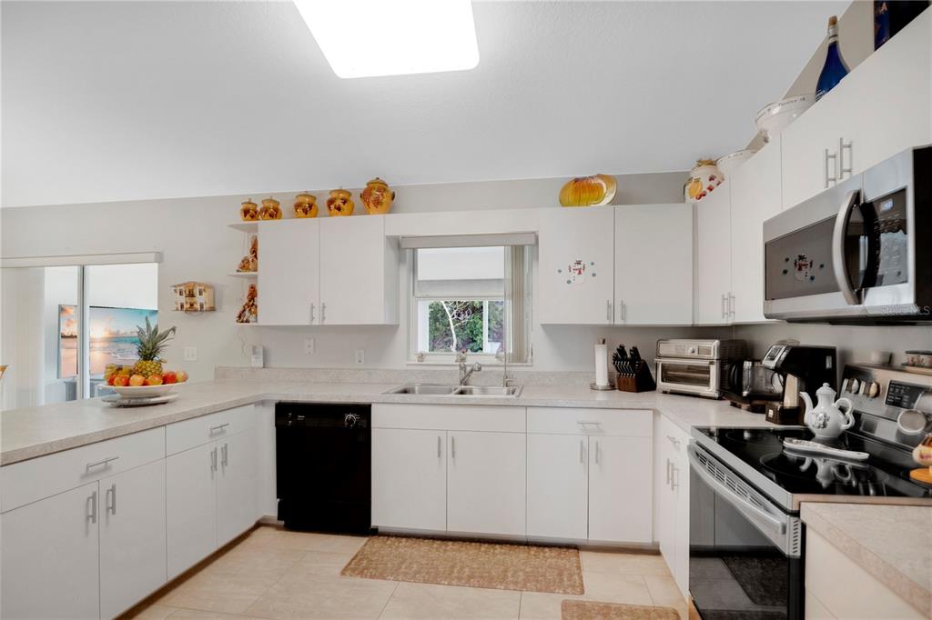 A kitchen features white cabinets, a black dishwasher, stainless steel appliances, and light countertops — 18 ANGELES ROAD, DEBARY, FL