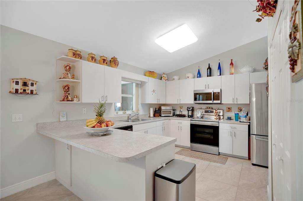 A kitchen features white cabinets, stainless steel appliances, a peninsula, and light-colored tile flooring — 18 ANGELES ROAD, DEBARY, FL