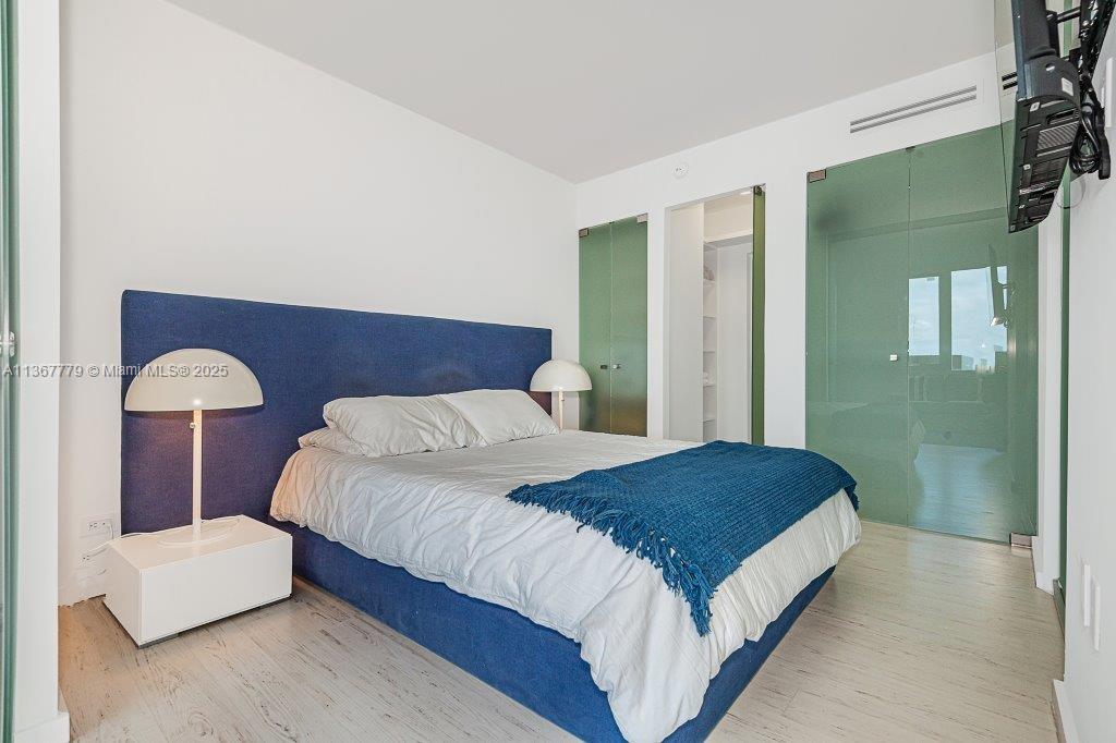 A bedroom features a blue upholstered headboard, white bedding, and green glass closet doors — 2301 Collins Ave # 1032, Miami Beach FL 33139, MIAMI BEACH, FL