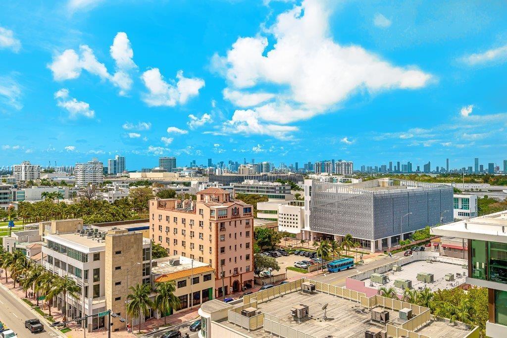 An elevated view of a city street with mid-rise buildings, palm trees, and a distant skyline — 2301 Collins Ave # 1032, Miami Beach FL 33139, MIAMI BEACH, FL