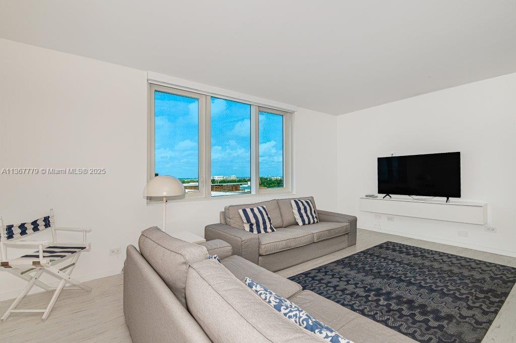A living room features a gray sofa, a patterned area rug, and a wall-mounted television — 2301 Collins Ave # 1032, Miami Beach FL 33139, MIAMI BEACH, FL