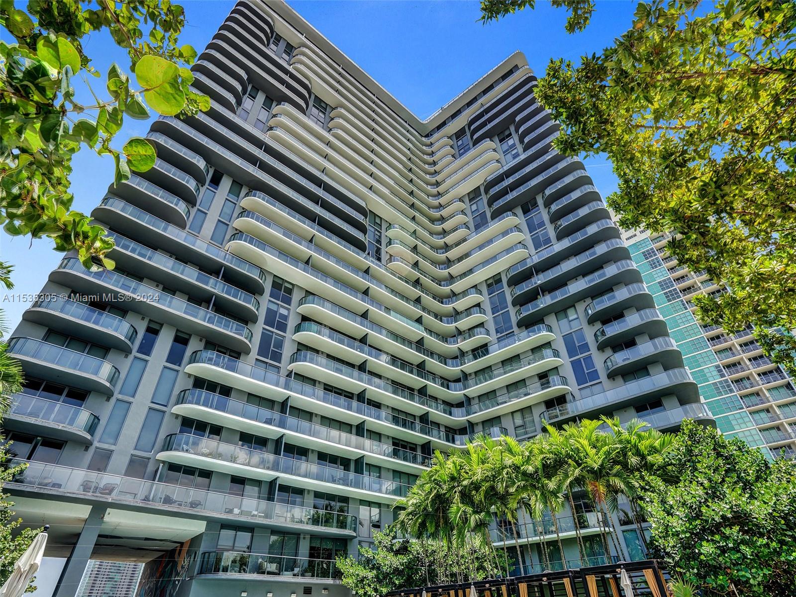 A low-angle view of a modern high-rise residential building with curved balconies and glass railings — 121 NE 34th St # 1801, Miami FL 33137, MIAMI, FL
