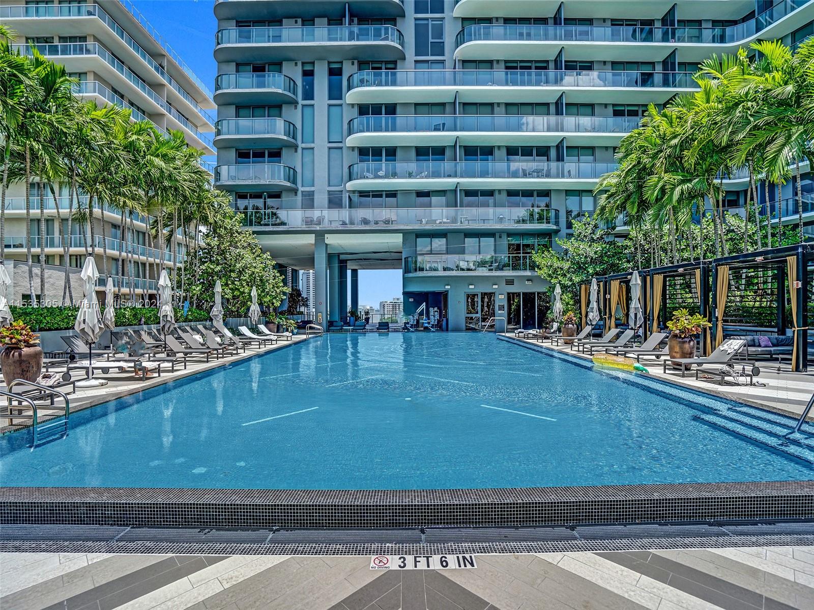 A rectangular swimming pool sits in a courtyard between two modern high-rise apartment buildings — 121 NE 34th St # 1801, Miami FL 33137, MIAMI, FL