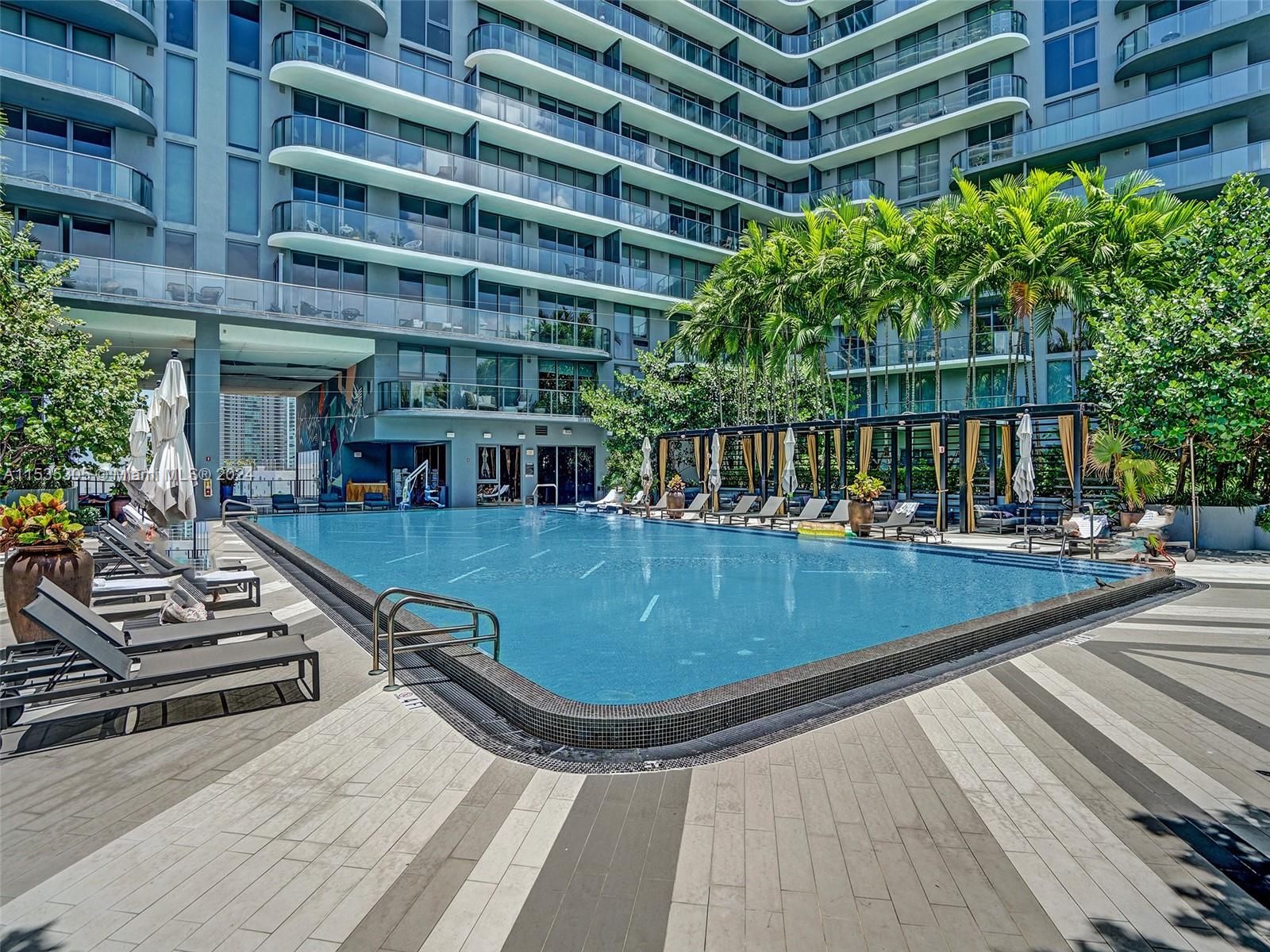 A large rectangular swimming pool sits on a patio surrounded by lounge chairs and palm trees — 121 NE 34th St # 1801, Miami FL 33137, MIAMI, FL