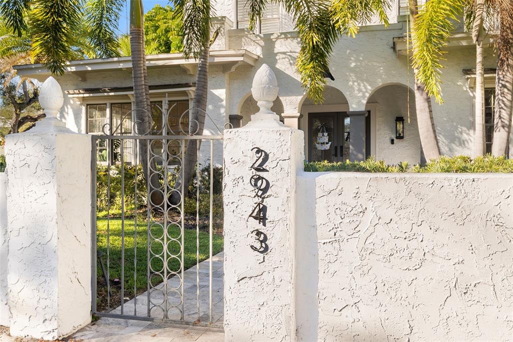 A white stucco wall with a metal gate and house numbers stands before a house — 2943 W BAYSHORE COURT, TAMPA, FL