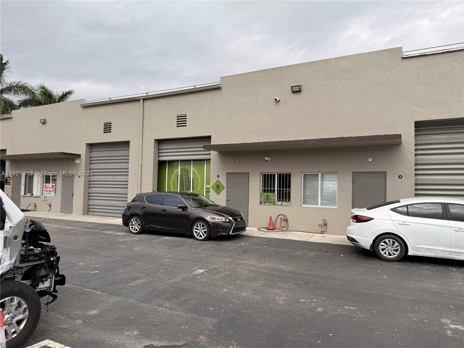 An exterior view of a commercial building with three garage doors and two parked cars — 16205 SW 117th Ave # 3, Miami FL 33177, MIAMI, FL