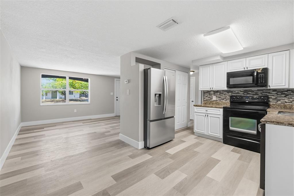 A kitchen with white cabinets and stainless steel appliances opens into a living area — 6150 EMERALD DRIVE, NEW PORT RICHEY, FL