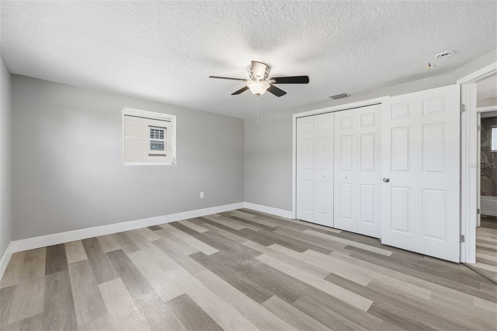 A bedroom with gray walls, wood-look plank flooring, a ceiling fan, and white closet doors — 6150 EMERALD DRIVE, NEW PORT RICHEY, FL