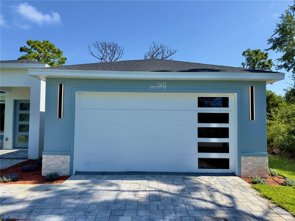 A blue exterior wall features a white garage door with vertical windows and stone accents — 140 LINDA LEE DRIVE, ROTONDA WEST, FL