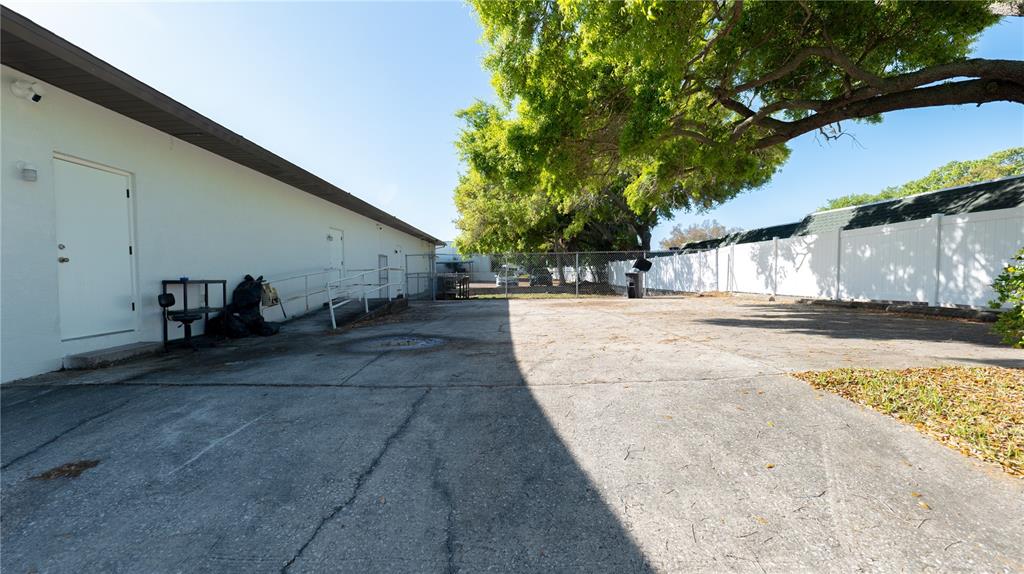 A paved exterior area features a white building wall, a metal ramp, and a fence — 190 PATRICIA AVENUE UNIT 3, DUNEDIN, FL