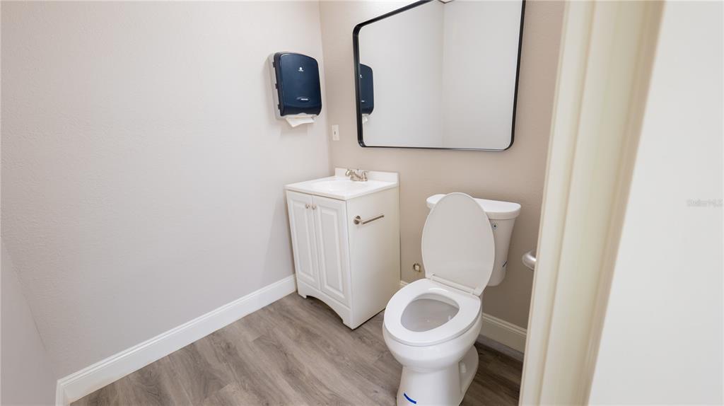 A small bathroom features a white vanity, a toilet, and a black-framed mirror — 190 PATRICIA AVENUE UNIT 3, DUNEDIN, FL