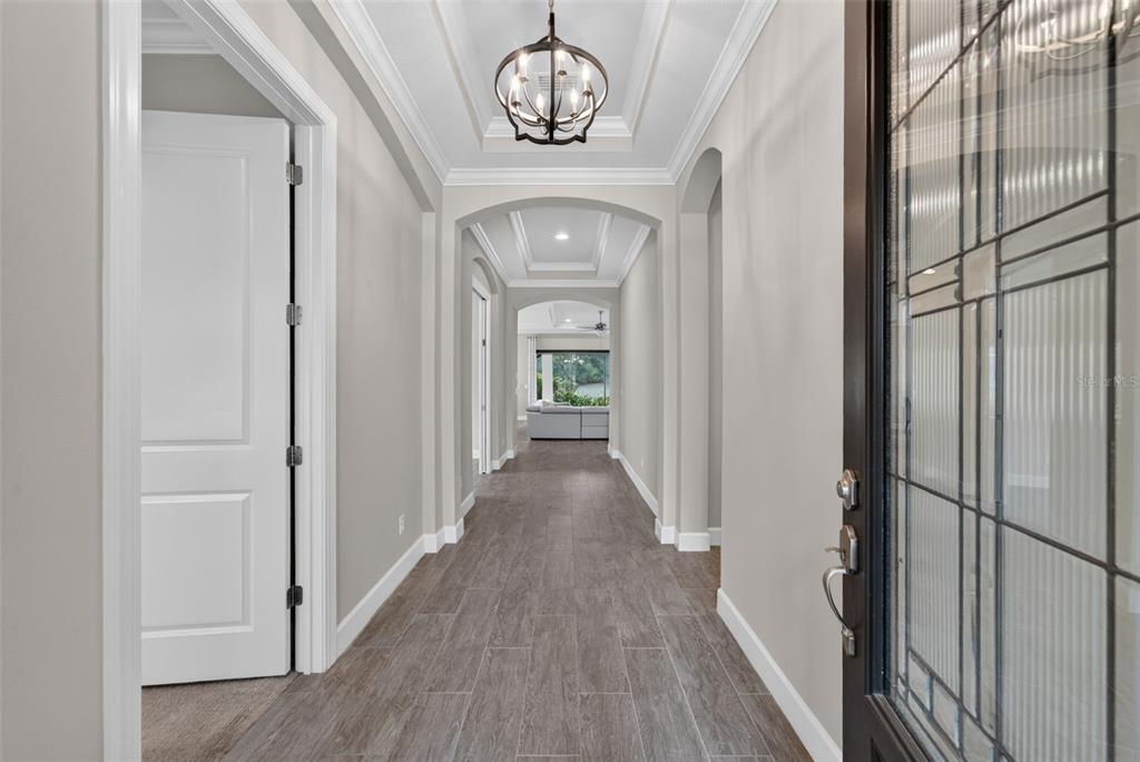A hallway with wood-look tile flooring leads toward a living area with a coffered ceiling — 12758 SORRENTO WAY, BRADENTON, FL