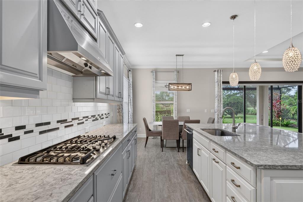 A kitchen features gray cabinets, a gas cooktop, a white island, and a dining area — 12758 SORRENTO WAY, BRADENTON, FL