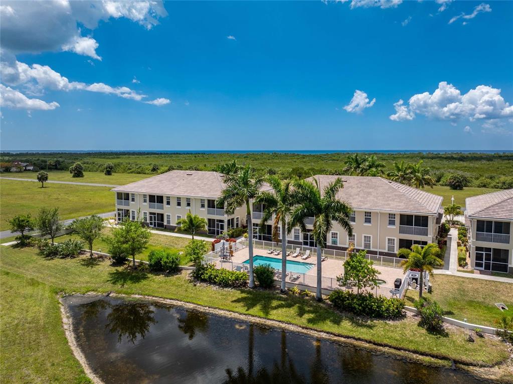 An aerial view of a multi-story apartment building with a pool and a small pond — 17094 ACAPULCO ROAD UNIT 321, PUNTA GORDA, FL
