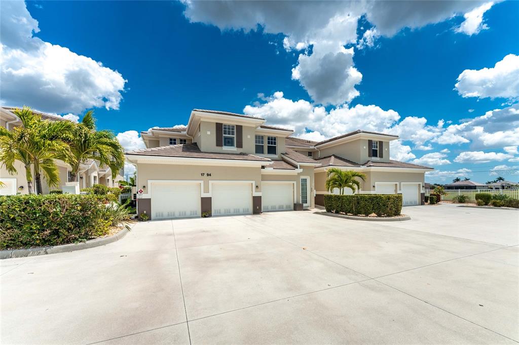 A multi-unit residential building with beige stucco walls, multiple garage doors, and palm trees — 17094 ACAPULCO ROAD UNIT 321, PUNTA GORDA, FL