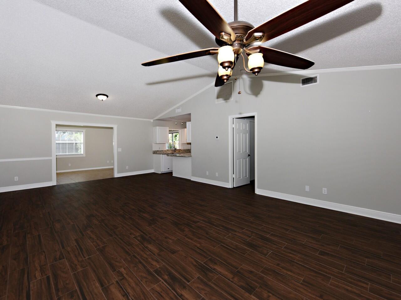 A spacious living room features dark wood-look tile flooring, a vaulted ceiling, and a ceiling fan — 598 NE Maranta Terrado, Jensen Beach FL 34957, JENSEN BEACH, FL