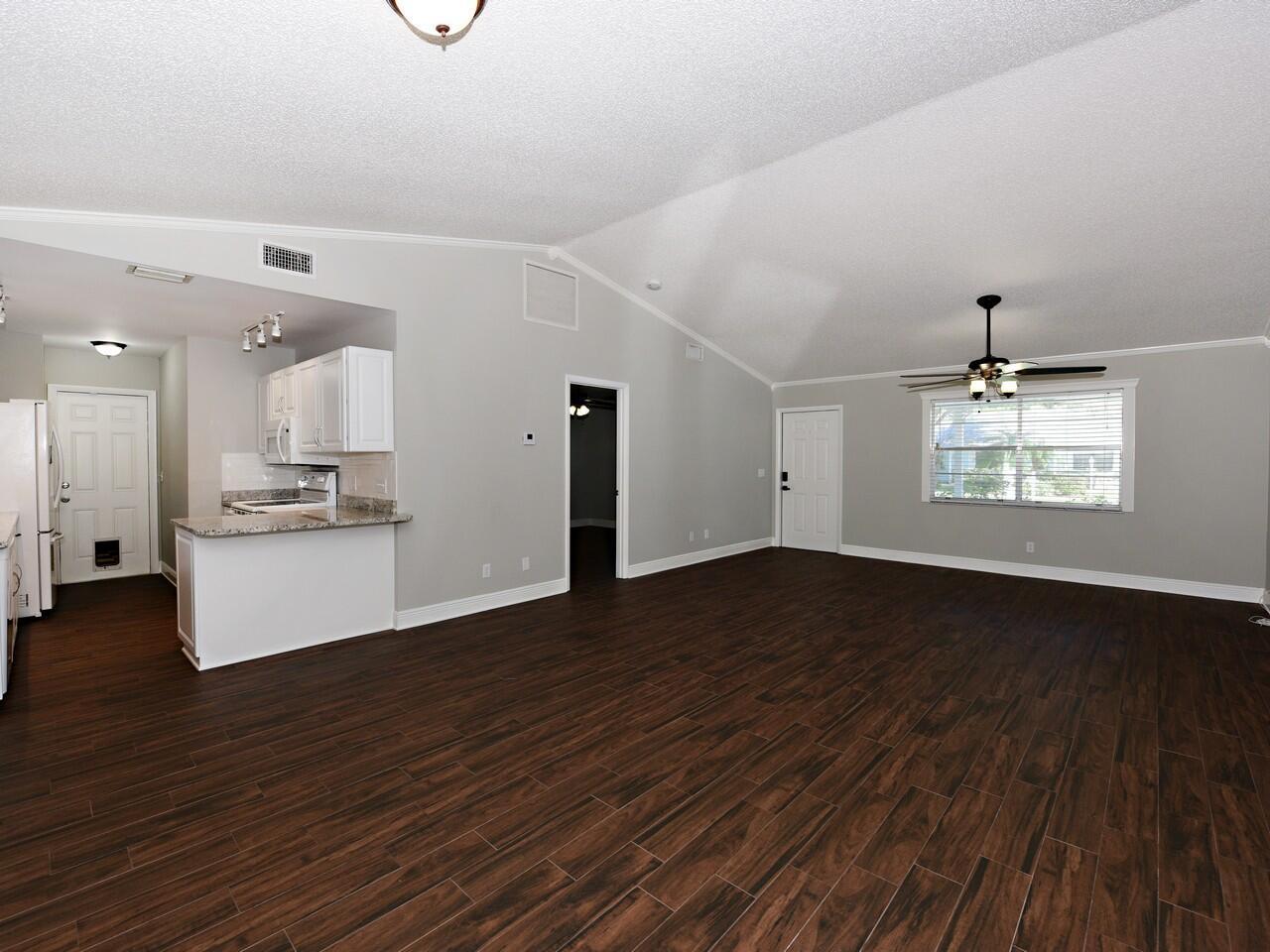 A spacious living room with vaulted ceilings, dark wood-look flooring, and an adjacent open kitchen — 598 NE Maranta Terrado, Jensen Beach FL 34957, JENSEN BEACH, FL