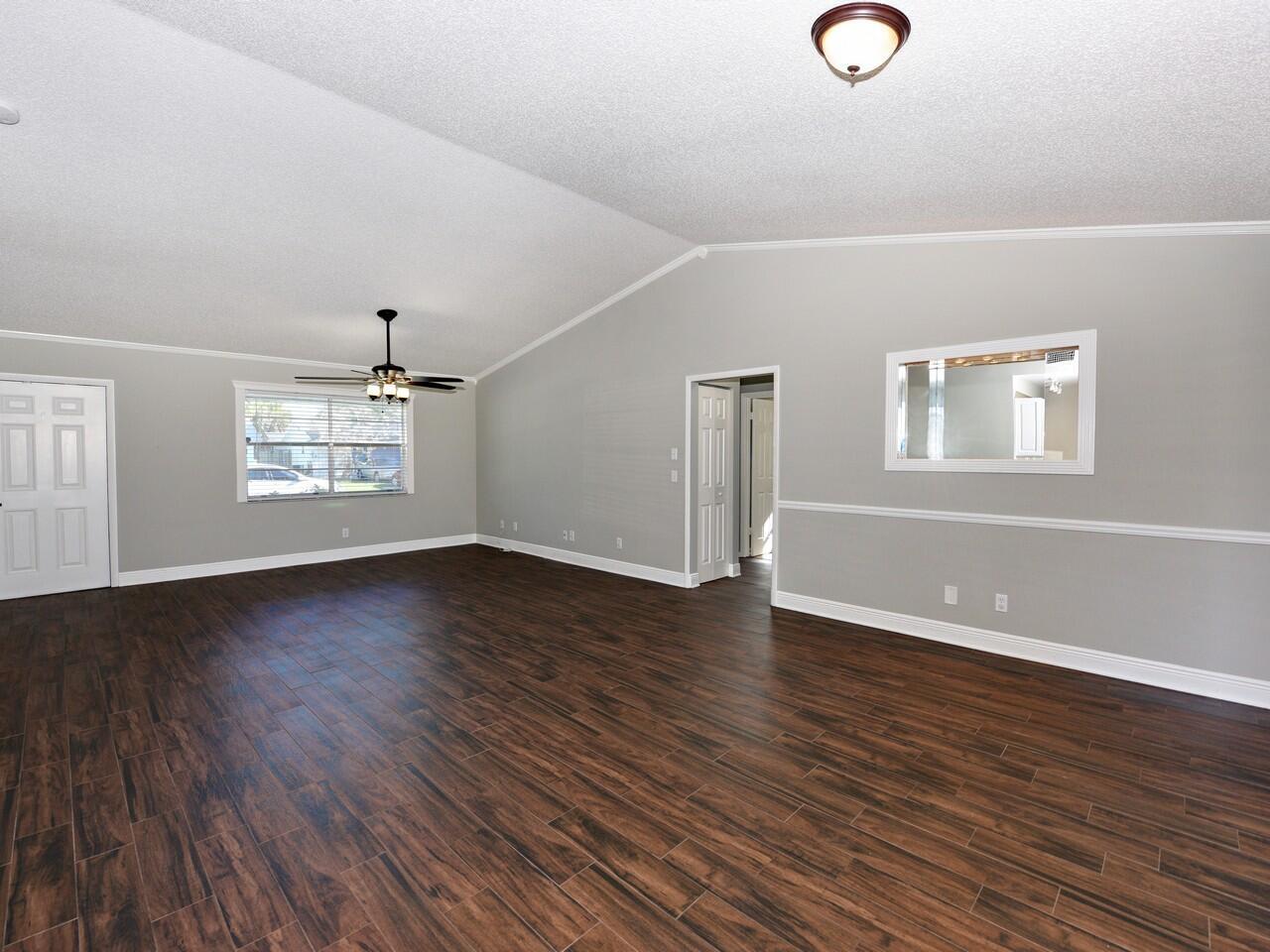 An empty living room features vaulted ceilings, dark wood-look tile flooring, and gray walls — 598 NE Maranta Terrado, Jensen Beach FL 34957, JENSEN BEACH, FL