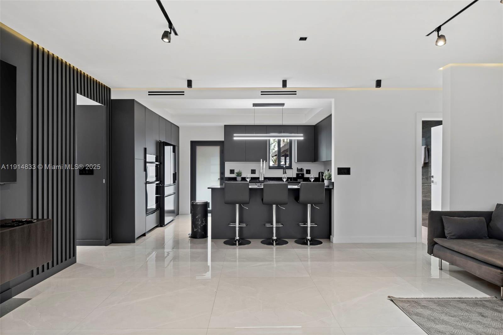 A modern kitchen features dark cabinetry, a breakfast bar with three stools, and tile flooring — 1101 N 14th Ave, Hollywood FL 33020, HOLLYWOOD, FL