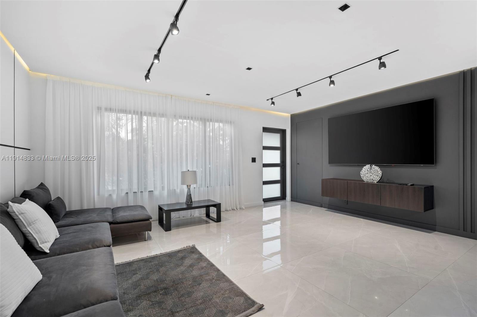 A modern living room features a grey sectional sofa, a wall-mounted television, and tile flooring — 1101 N 14th Ave, Hollywood FL 33020, HOLLYWOOD, FL