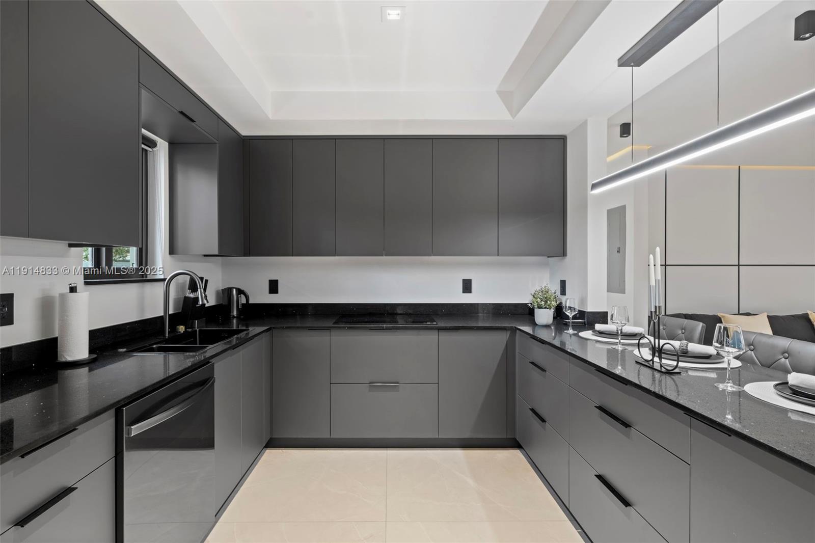 A modern kitchen features dark gray cabinetry, black countertops, and a linear pendant light — 1101 N 14th Ave, Hollywood FL 33020, HOLLYWOOD, FL