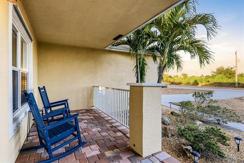 A covered porch features blue rocking chairs on a brick paver floor with palm trees — 10379 CALUMET BOULEVARD, PORT CHARLOTTE, FL