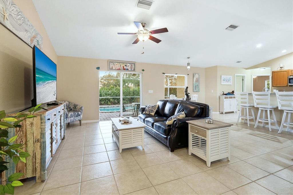 A living room features a vaulted ceiling, tile flooring, a television console, and a sofa — 10379 CALUMET BOULEVARD, PORT CHARLOTTE, FL