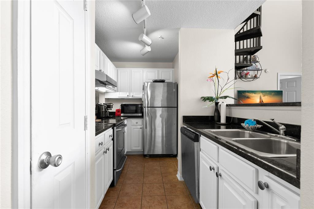 A galley kitchen features white cabinets, stainless steel appliances, black countertops, and tile flooring — 501 KNIGHTS RUN AVENUE UNIT 1310, TAMPA, FL