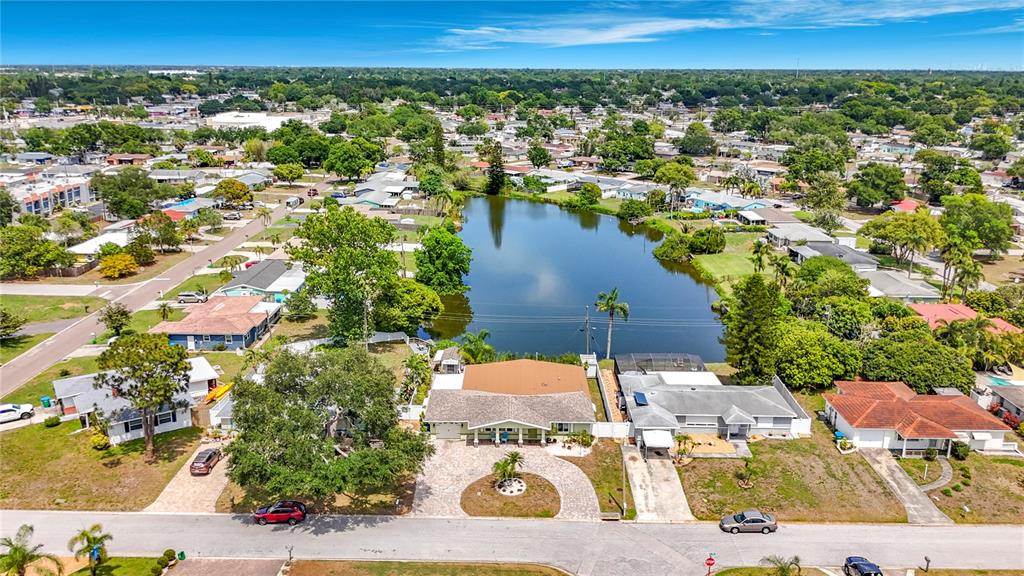 An aerial view shows a residential neighborhood with houses situated along a small lake — 5163 60TH WAY N, KENNETH CITY, FL