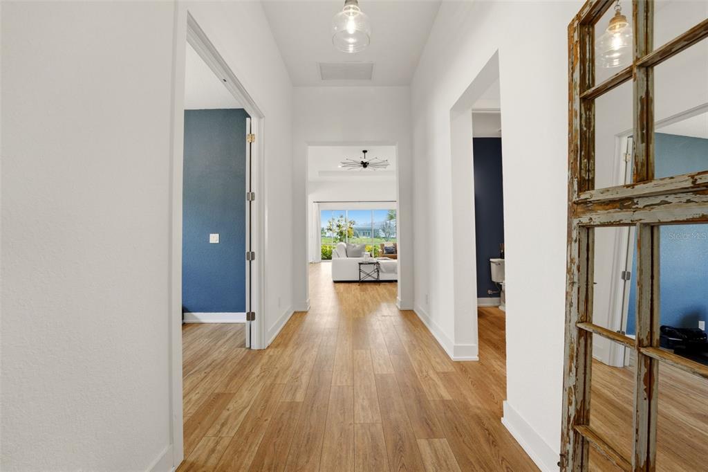 A hallway with wood-look flooring leads to a living area with a view of outdoors — 7857 REDONDA LOOP, LAKEWOOD RANCH, FL