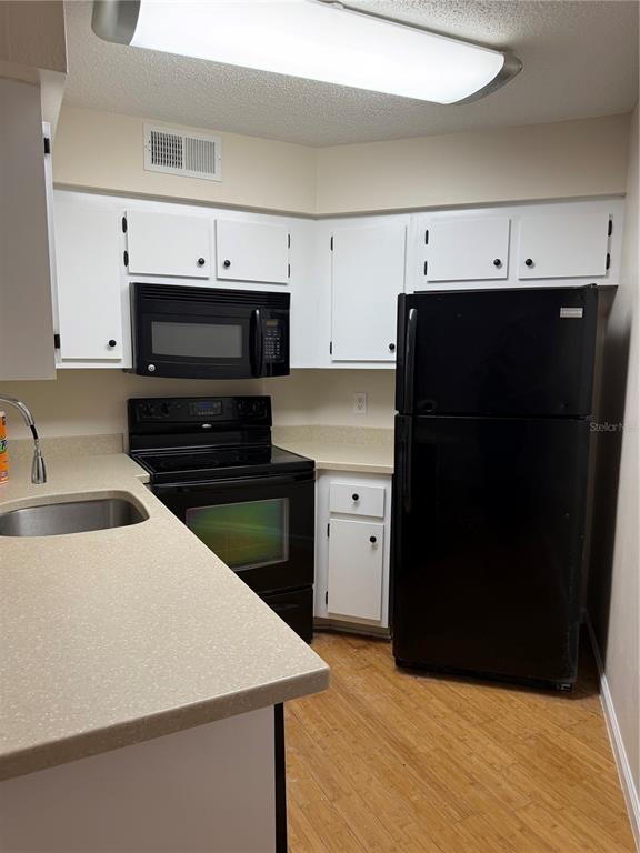 A kitchen features white cabinets, black appliances, tan countertops, and light wood-look flooring — 3816 SOUTHPOINTE DRIVE UNIT U2, ORLANDO, FL