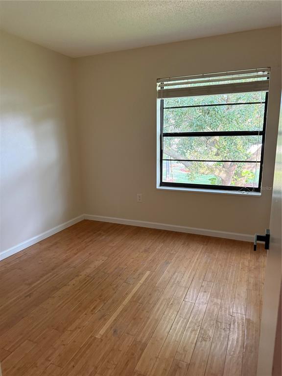 An empty bedroom features light-colored walls, wood-look flooring, and a window overlooking a tree — 3816 SOUTHPOINTE DRIVE UNIT U2, ORLANDO, FL